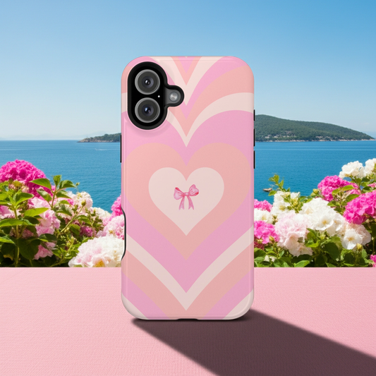 Phone case with heart design and bow on a pink surface with flowers and ocean in the background
