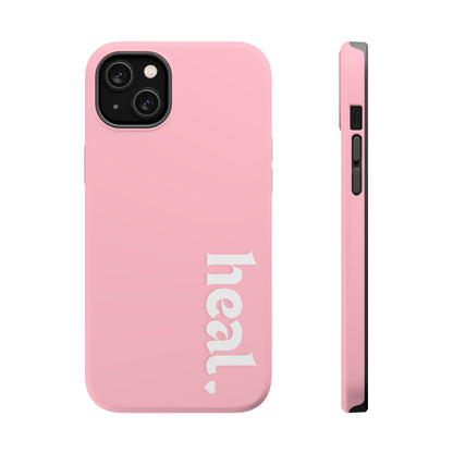A pink iPhone case with the word 'heal' written on it, displayed on a table with candles and flowers in the background.