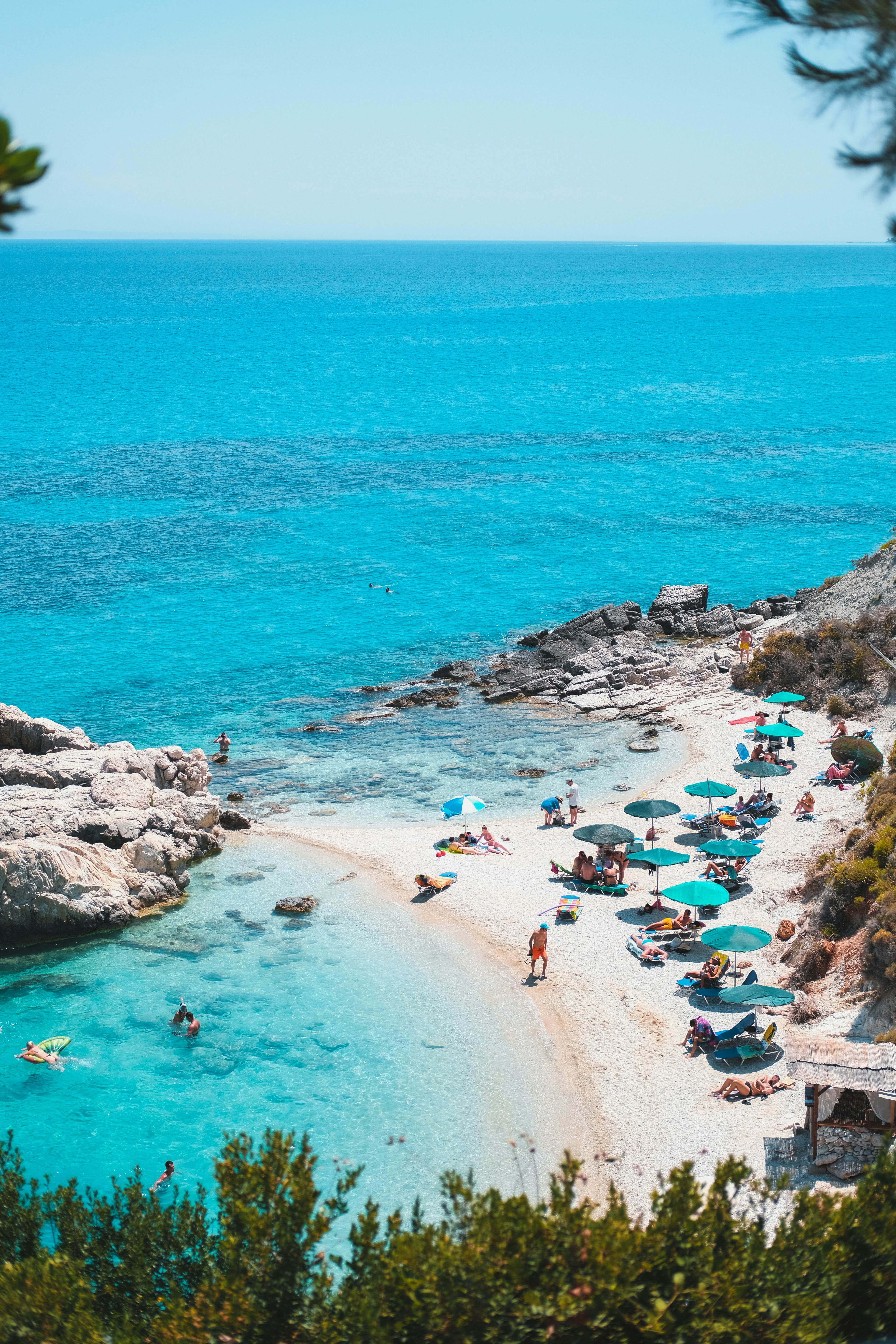 Beach scene with clear blue water, rocky shoreline, and people enjoying the sun.